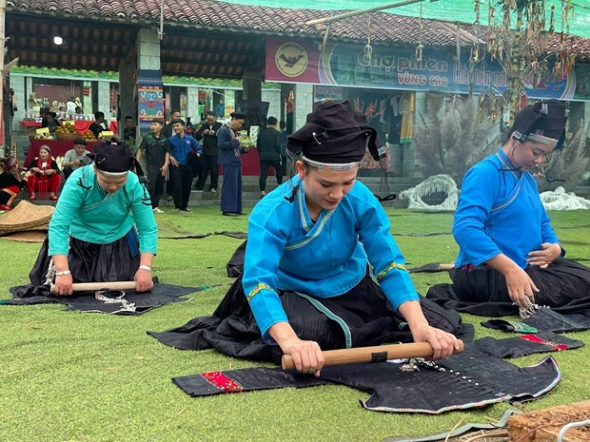 Đồng bào dân tộc Nùng trình diễn công đoạn chà bóng vải đen để may trang phục đặc sắc của dân tộc mình. Ảnh: Hoàng Tâm