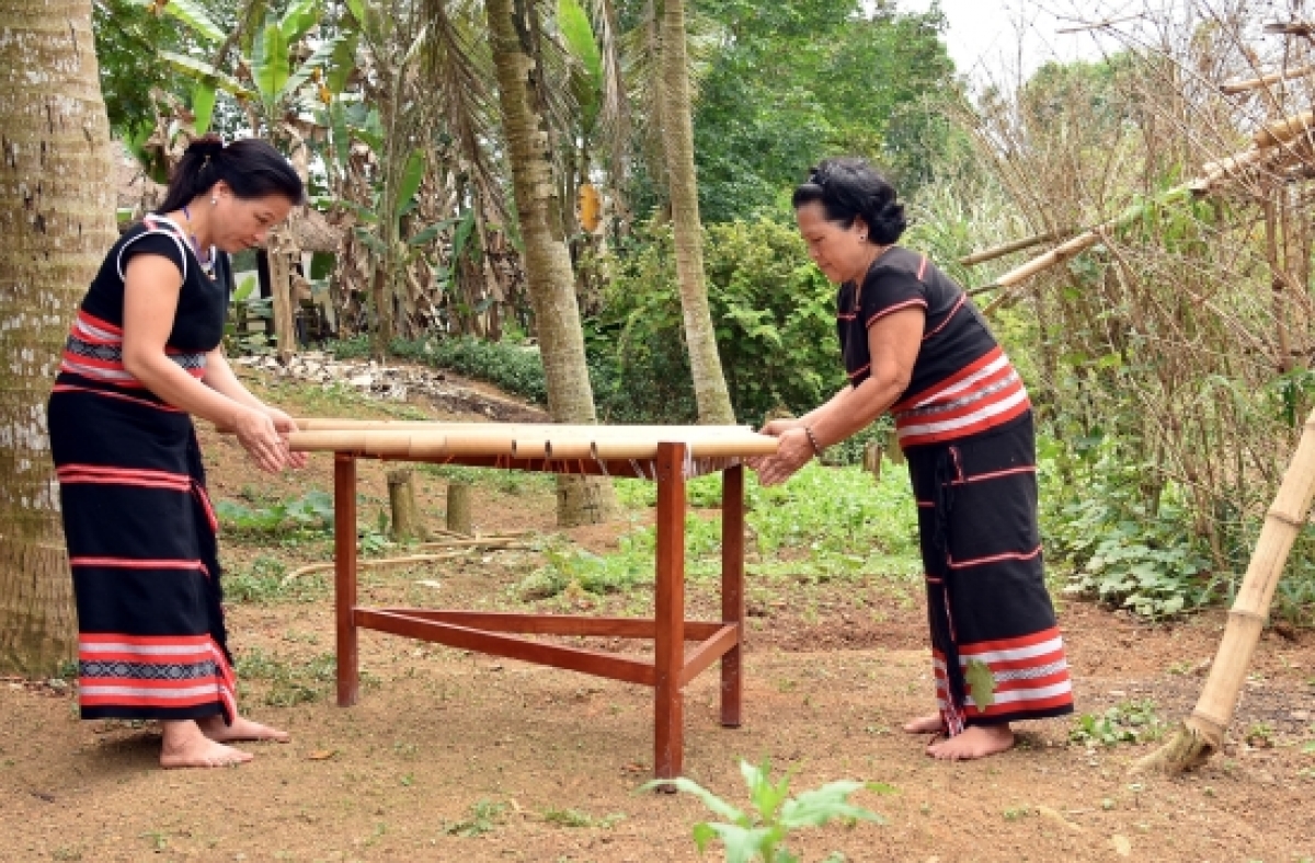 Nghệ nhân Y Sinh (phải) dạy cô gái người Xơ Đăng “vỗ” đàn Klông Pút. Ảnh: Thanh Thuận  - Báo Biên phòng