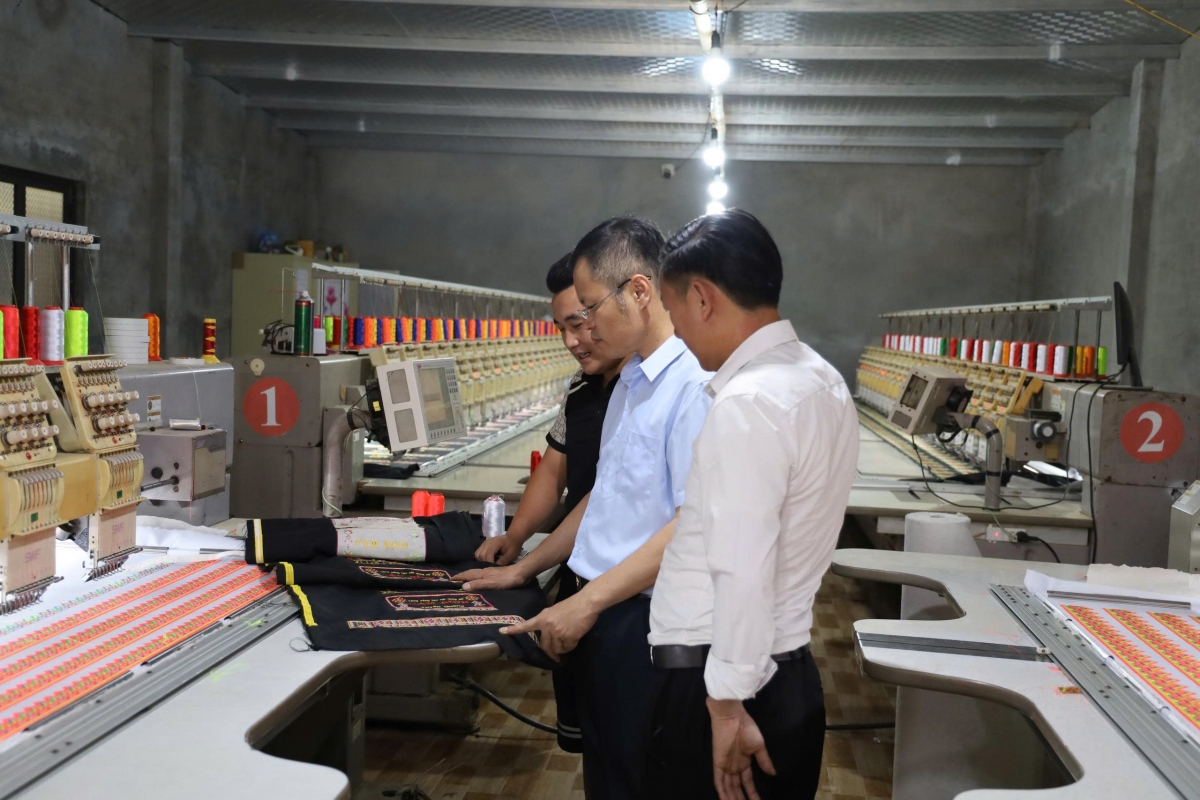 Giàng A Hồng (áo đen) giới thiệu sản phẩm thổ cẩm do xưởng sản xuất của mình tạo ra (Ảnh: Đinh Tuấn)